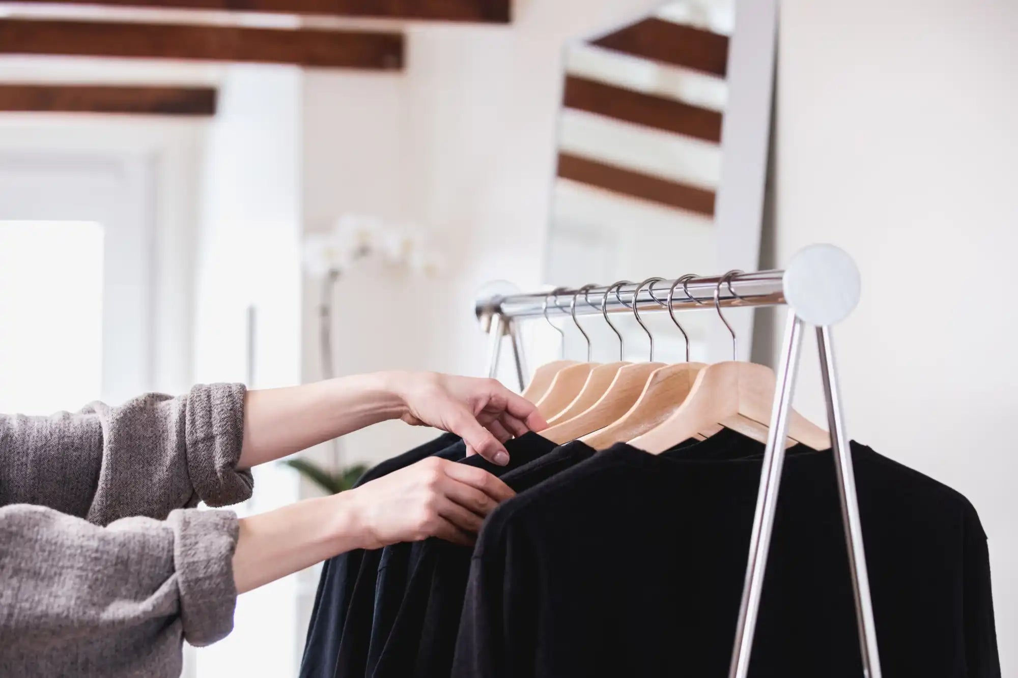 Hands sorting through clothing on a garment rack.